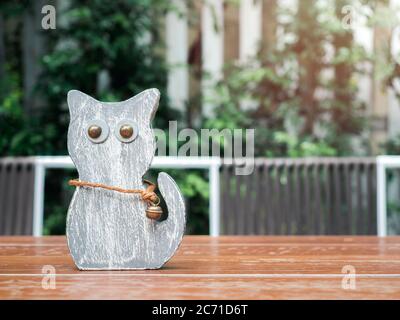 Cute cat wooden doll with big eyes and bell on wooden table on green bush background. Stock Photo