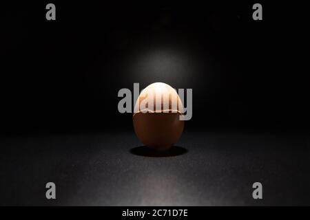 Broken chicken eggshell isolated on black background with copy space. Light filters through the cracks. Stock Photo