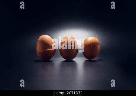 Three broken chicken eggshells in line isolated on black background with copy space. Light filters through the cracks. Stock Photo