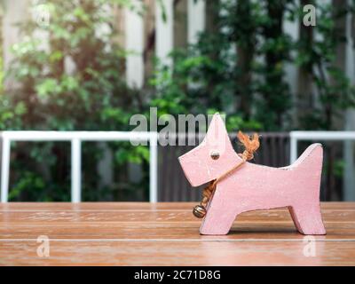 Cute pink dog wooden doll with big eyes and bell on wooden table on green bush background. Stock Photo