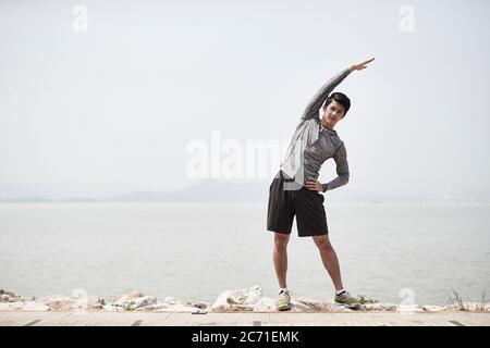 young asian adult man stretching body outdoors by the sea