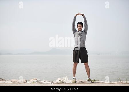 young asian adult man stretching arms outdoors by the sea