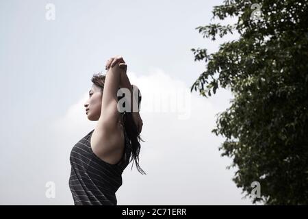 young asian adult woman stretching arms outdoors, low angle side view