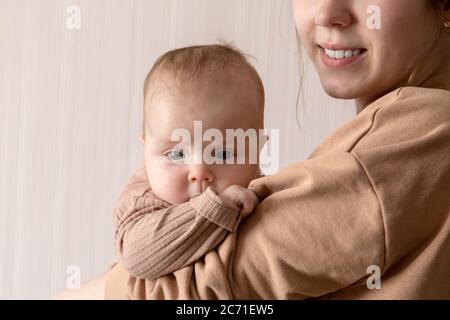 A young mother holds a child girl who is 3 months old. The brooding child in his mother's arms looks into the camera.  Stock Photo