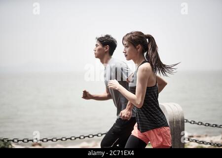 young asian man and woman running jogging outdoors by the sea, side view