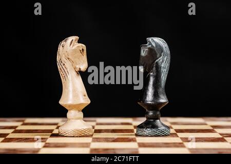 pieces of knights facing each other on a chessboard against a black background Stock Photo