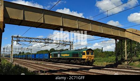 Freightliner diesel locomotive no 66524 passes under a foot bridge to the south of Acton Bridge station on train of empty refuse from Runcorn. Stock Photo