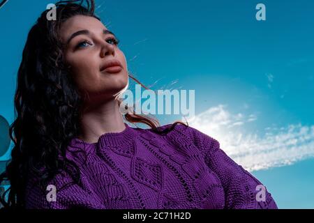 Attractive Woman With Curly Hair at Blue Bright Sky Background. Summer Cotton Knitted Violet Sweater or Jumper Stock Photo