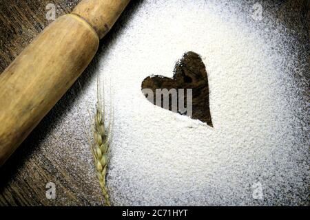 Fresh harvested wheat grain on wheat flour background. sprinkled flour with heart. Heart drawn in scattered flour alongside a wooden rolling pin. Stock Photo