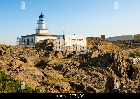 view of cap de creus lighthouse, a beacon of light on the rocky catalan costa brava, on a sunny summer day at sunset with warm light and wind blowing Stock Photo