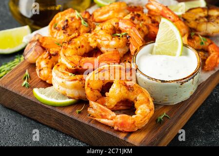 Grilled shrimps or prawns served with lime, garlic and white sauce on a dark concrete background. Seafood Stock Photo