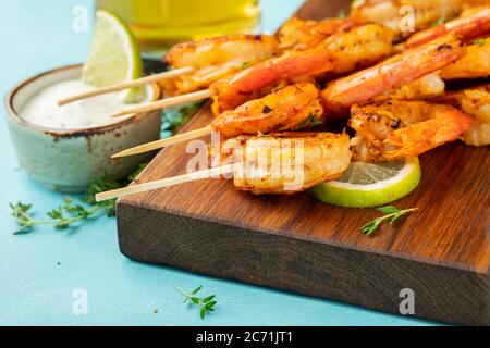 Grilled shrimp skewers or langoustines served with lime, garlic and sauce on a light blue concrete background. Seafood Stock Photo