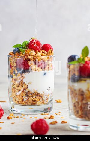Yogurt parfait with granola, raspberries and blueberries in glasses, light background. Healthy breakfast concept. Stock Photo