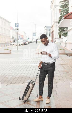 Young handsome black man with luggage using smartphone and listening music with earphones in the city Stock Photo
