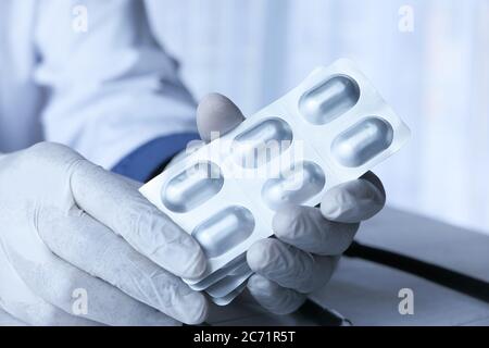Close up of doctor hand in protective gloves holding blister pack  Stock Photo