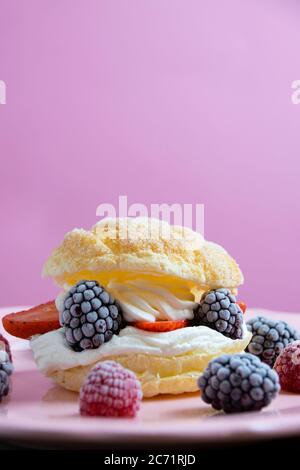 Vertical photography of puff pastry filled with whipped cream, raspberries, blackberries and strawberries on a pale pink plate on a light pink backgro Stock Photo