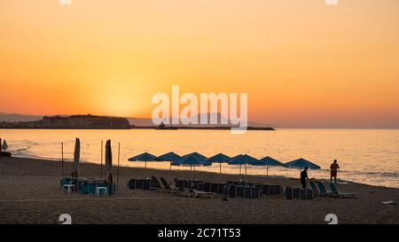 Sun setting over umbrella filled beach at the Mediterranean Sea in Crete, Greece Stock Photo