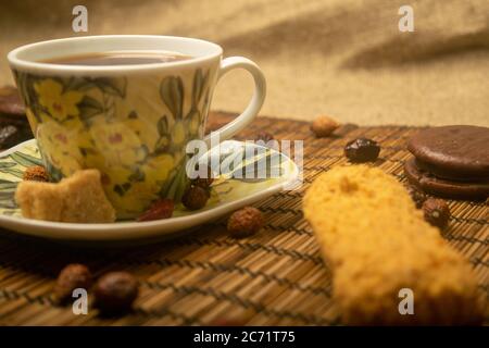 A Cup of tea, dried rosehip fruit, pieces of brown cane sugar, and cookies on a reed Mat. Close up Stock Photo