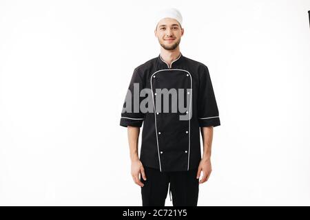 Young man chef in black uniform and white cap dreamily looking in camera over white background Stock Photo
