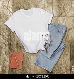 White tshirt mockup fashion clothing.   Gray pants, white shirt, leather diary and pen and a boho necklace on a wood background with room for text for Stock Photo