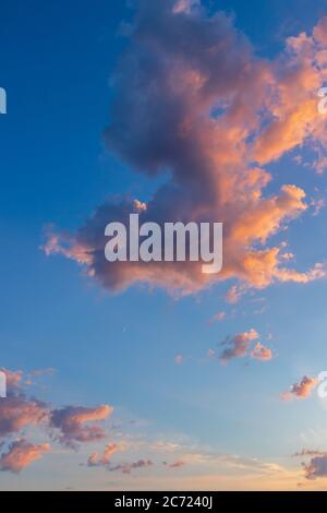 Dramatic fluffy Cumulus clouds at sunset with golden light at cloud edges. Vertical image with far off crescent moon Stock Photo