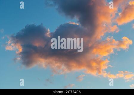 Dramatic golden Cumulus clouds at sunset with bright orange yellow light as sun sets in blue heavenly sky Stock Photo