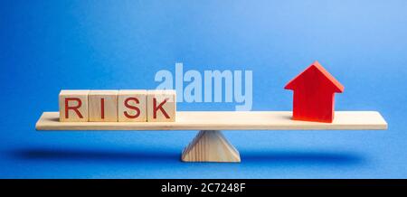 The word risk and a miniature house on the scales. The concept of mortgage, loans and real estate. Taxes and debts. Property insurance Stock Photo