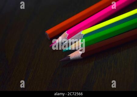 Five different colored wood pencil crayons placed on top of one another on a desk Stock Photo