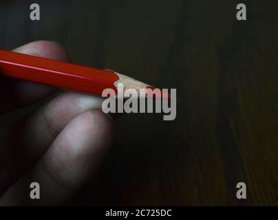 Person holding a red color wood pencil crayon with his hand on a brown color desk Stock Photo