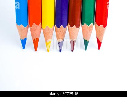 Seven different colored wood pencil crayons placed in line on a white paper background Stock Photo