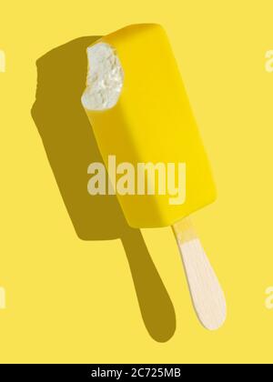 Bitten yellow ice cream bar with lemon taste on a stick on yellow background; full depth of field Stock Photo