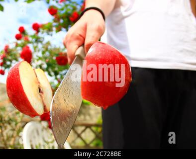 An red apple cut in half with a kitchen knife. Summer vitamin fruit. Food for vegan and vegetarian. Background blurred voluntarily. Stock Photo