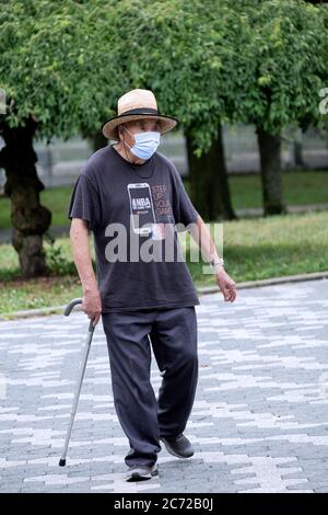 An Asian American senior citizen exercise walks with a cane and while wearing a surgical mask. In Kissena Park, Flushing, Queens, New York City. Stock Photo