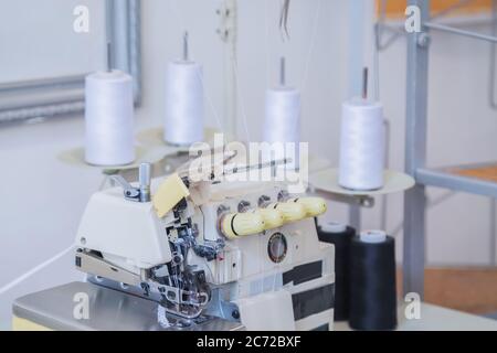 Overlocking sewing machine on table in bright room at atelier. Fashion, equipment for sewing, needlework, manufacturing, tailoring, hobby, clothing Stock Photo