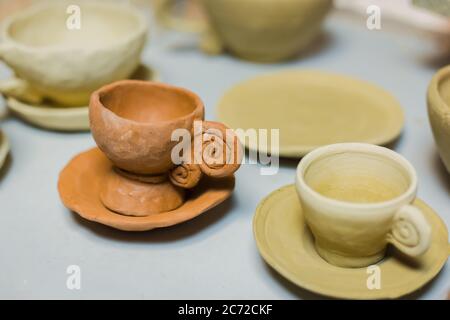 Unfinished tea cups on shelf of pottery workshop, ceramic studio - close up view. Crafting, DIY, artwork and handmade concept Stock Photo