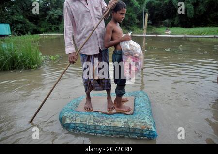 People on a handmade raft out of plastic in Sadarpar, Uposhahar. The area is submerged with water due the recent floods from the heavy rainfall triggered during the monsoon season over the last few days. Bangladesh is also heavily hit by the coronavirus pandemic. Sylhet, Bangladesh. Stock Photo