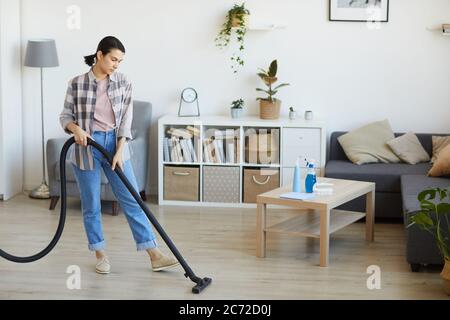 Young housewife vacuuming the floor in the living room at home she doing housework Stock Photo