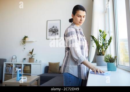Young woman doing chores she wiping the dust from the windowsill in the room Stock Photo