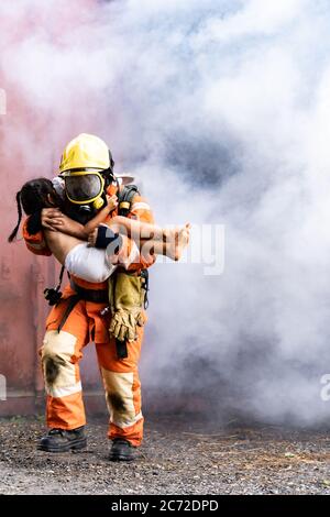 Firefighter rescue girl little child from burning building. He hold the girl and run out through smoke from building. Firefighter safety rescue from a Stock Photo