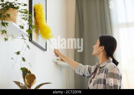 Young woman working at home she wiping dust from pictures on the wall Stock Photo