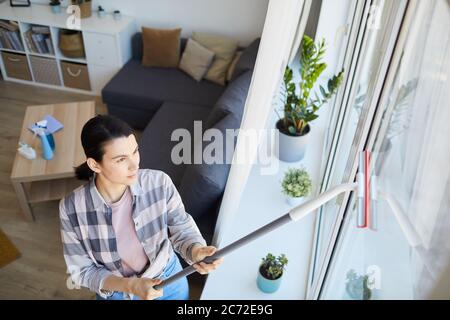 Young woman using sponge and cleaning the window in the room at home Stock Photo