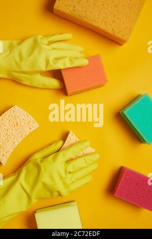 Close-up of woman in rubber yellow gloves using sponges for cleaning isolated on yellow background Stock Photo