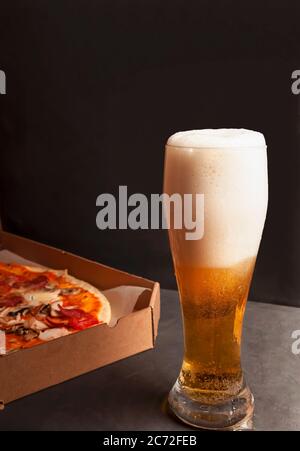 Beer with a large mouth-watering foam and pizza from delivery in craft packaging from delivery in the background. Design element. Glass of craft beer Stock Photo
