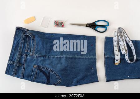Just cutted blue denip shorts, measuring tape, scissors and sewing pin on a white table. Shorten the jeans with scissors and sewing pin. DIY. Stock Photo