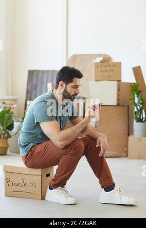 Young bearded man sitting on the box and using his mobile phone during relocation Stock Photo