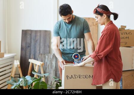 Young couple packing things in the boxes and using adhesive tape during relocation Stock Photo