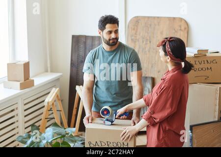 Young couple packing things in cardboard boxes and discussing something during moving in new apartment Stock Photo