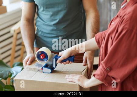 Close-up of young couple packing things in boxes together and using adhesive tape during moving in house Stock Photo