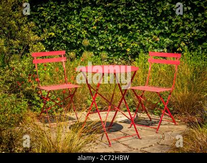 Red metal bistro table with two chairs on a circular stone patio. Stock Photo