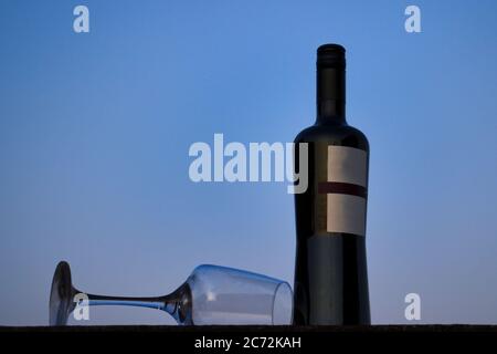 Bottle of red wine with a glass lying beside, under a blue sky Stock Photo